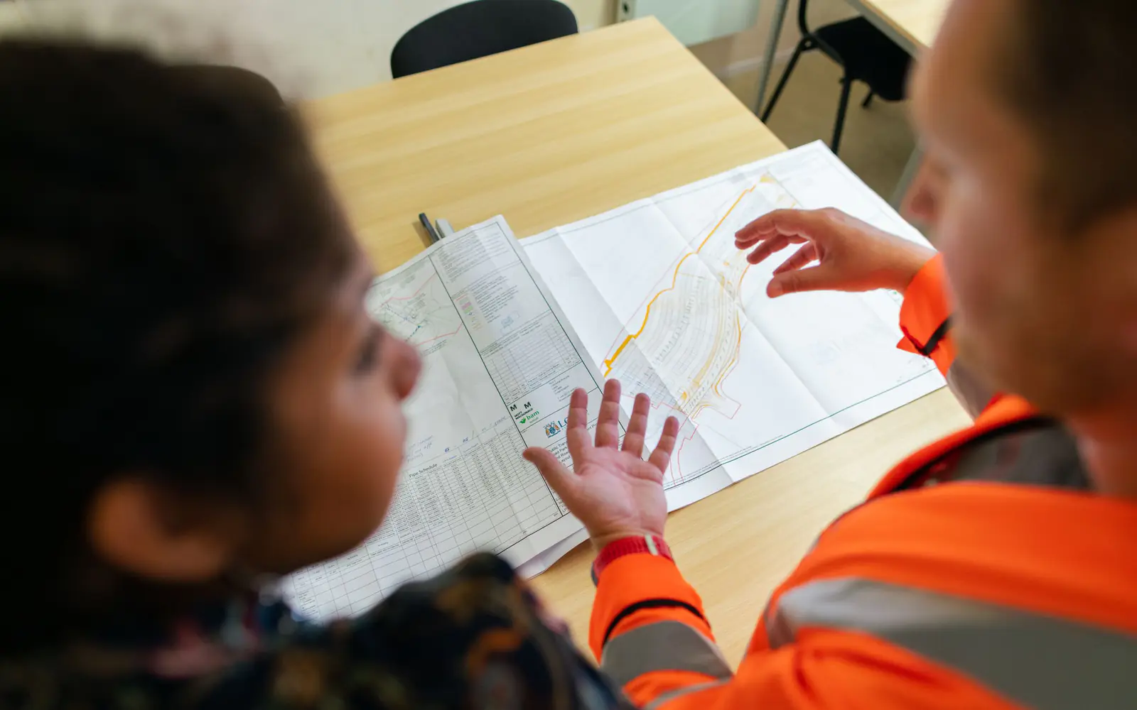 Two engineers in high-visibility clothing reviewing a drawing together
