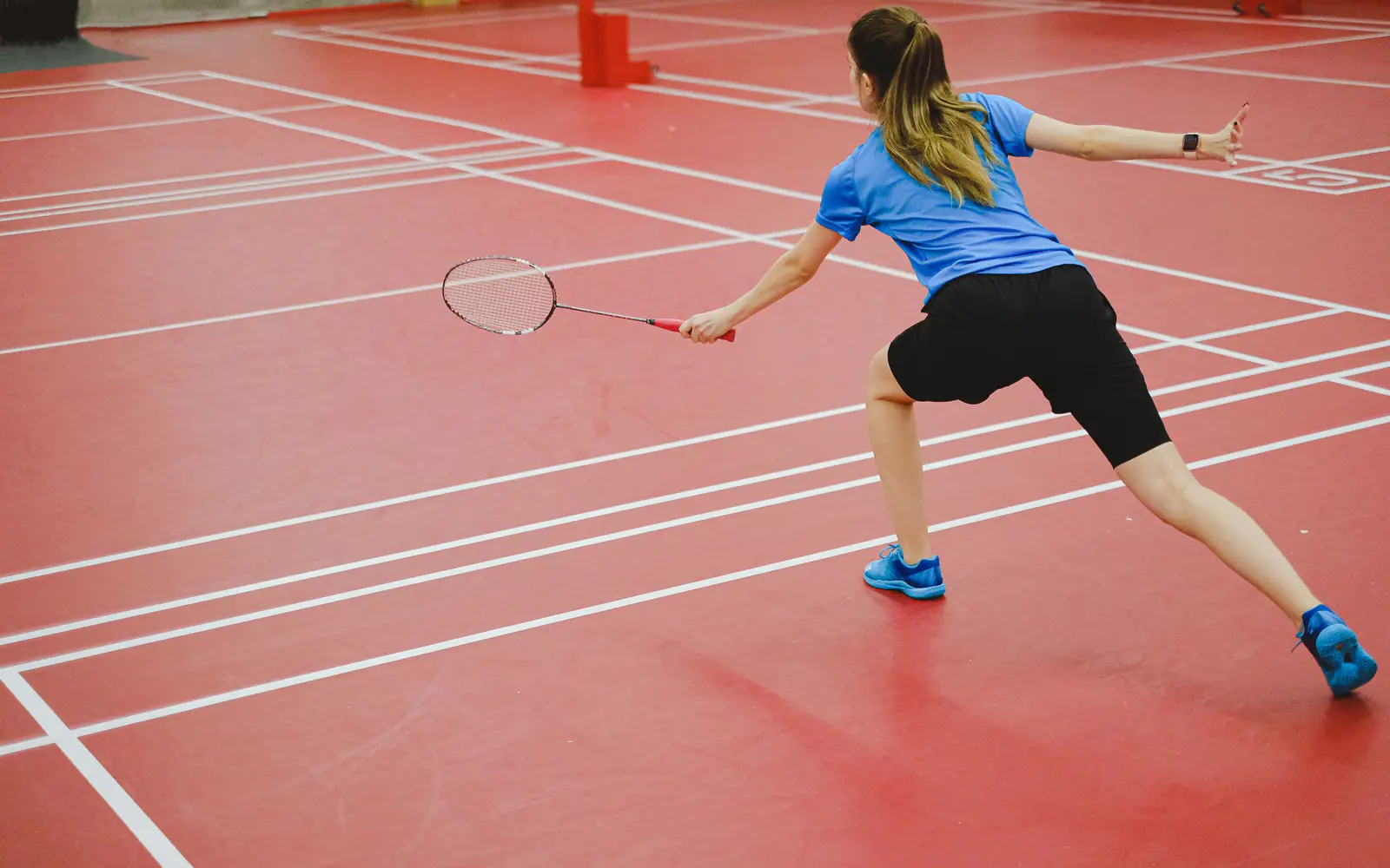 A player mid-rally on an indoor badminton court