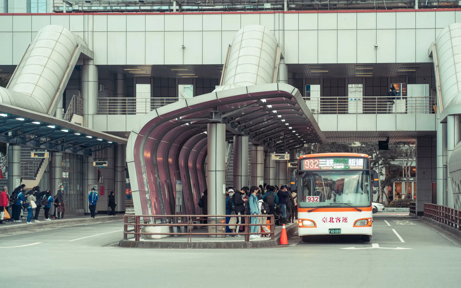 Passengers boarding beneath the covered concourse of a city bus terminal