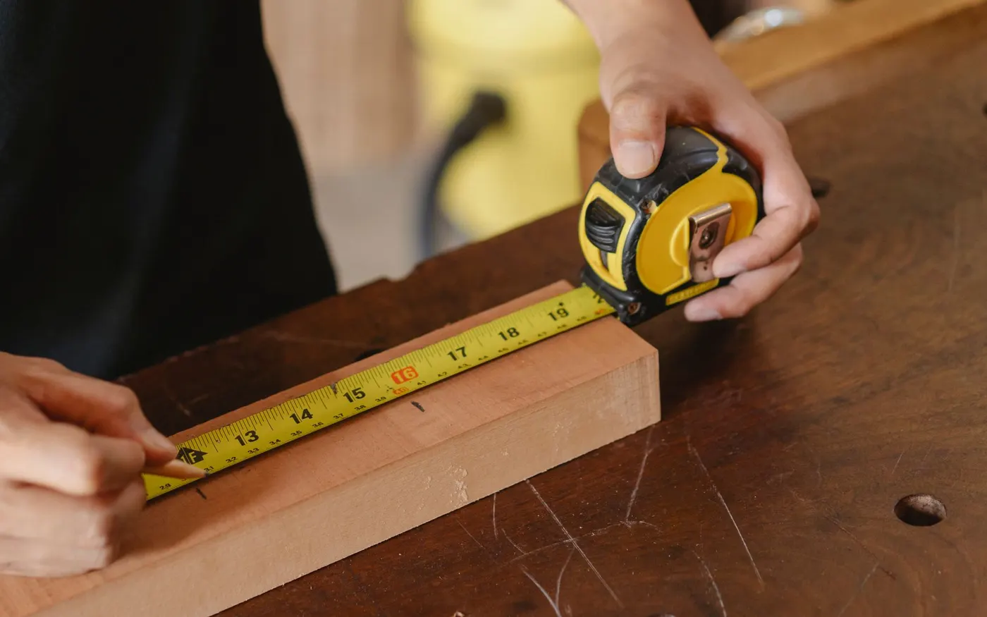 A worker marking a measurement on timber with a tape measure and pencil