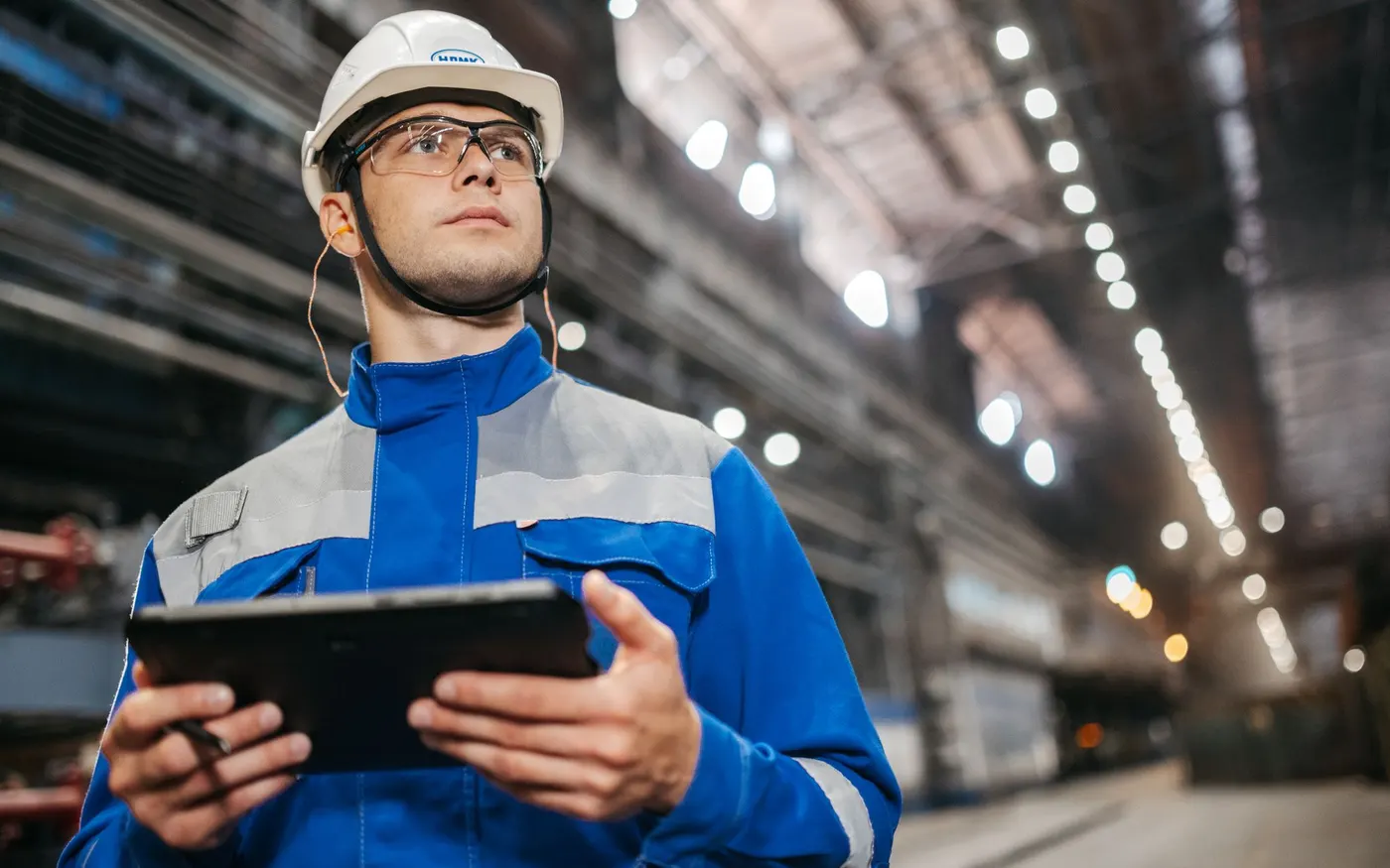 A worker in safety gear using a tablet in an industrial setting
