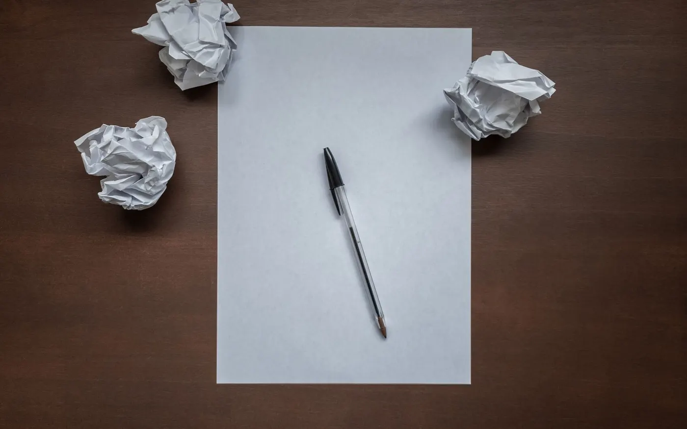 Crumpled paper balls beside a pen on a desk