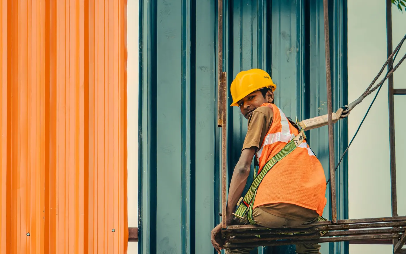 A worker in a helmet and vest moving across scaffolding